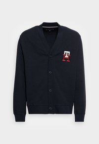 Cardigan blu navy realizzato in tessuto morbido, con scollo a V, chiusura frontale con sei bottoni e logo ricamato in rosso e bianco sul petto a sinistra.