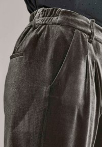 Nahaufnahme von dunkelgrauen Samenhosen mit elastischem Bund sowie seitlichen und hinteren Taschen, getragen mit einem schwarzen Oberteil.