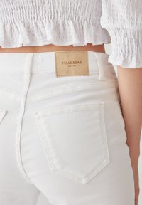 Jean en denim blanc avec un patch en cuir portant le label "PULL&BEAR denim", accentué par des poches arrière doubles et une coupe ajustée.