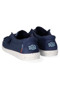 Bottines bleu marine sans lacets avec un dessus tissé respirant, tissu texturé et une semelle blanche mouchetée. Présente le logo "HEY DUDE" au talon.