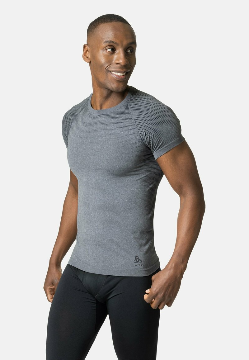 Camisa deportiva gris de manga corta con textura de malla en los hombros, combinada con mallas de ciclismo negras. Diseño ajustado, tela suave.