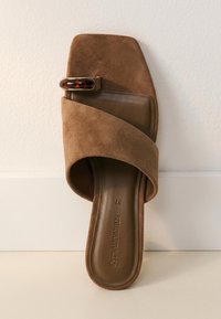 Brun ruskind slip-in sandal med bred rem, skildpaddemønstret spænde og firkantet tåkappe design på en lys baggrund.