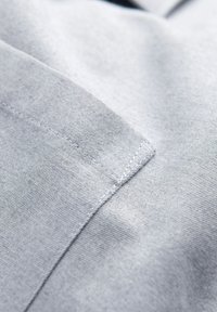 Gros plan sur un tissu gris clair montrant les coutures détaillées et les bords de couture d'un vêtement.