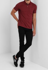 Camisa polo marrón de manga corta, con detalle de bolsillo, combinada con jeans negros ajustados y zapatillas negras con acentos blancos.