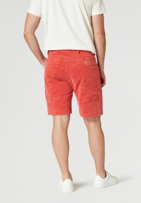 Röda velourshorts med sidofickor och en bakficka, kombinerade med vita sneakers. Slät textur, knälång design.