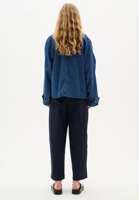 Džínová bunda v tmavě modré barvě, s oversized střihem, spadlými rameny a knoflíkovými manžetami. V kombinaci s námořnickými zúženými kalhotami a černými sandály.