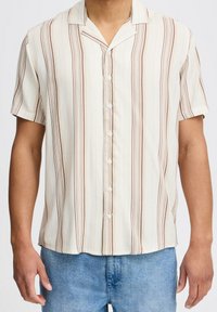 Camisa de botones de manga corta en tejido ligero, con rayas verticales en crema y marrón, cuello de campamento y botones pequeños.