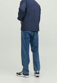 Marinkviltad jacka, blå denimjeans och svarta sneakers med grå detaljer. Fokusera på rena linjer och avslappnad stil.