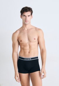 Boxer-briefs noirs avec une ceinture logotypée. Le tissu semble lisse et extensible, conçu pour une silhouette ajustée.