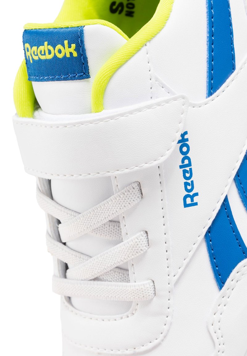 Baskets Reebok blanches avec logo et bande bleus, lacets blancs, strap velcro, et doublure intérieure jaune vif visible au niveau du col de la cheville.