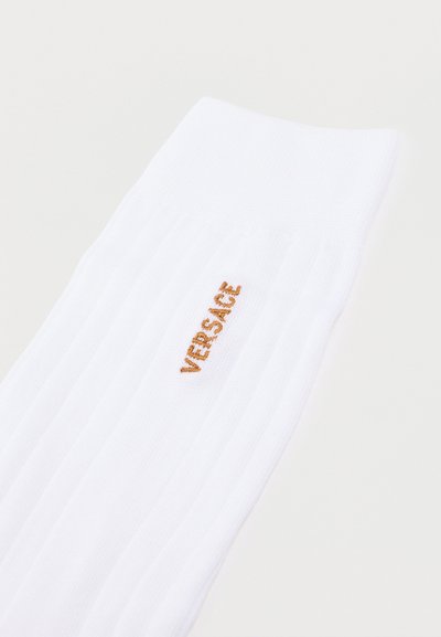 Λευκή ριμπ κάλτσα με μικρό κάθετο χρυσό λογότυπο "VERSACE" κεντημένο κοντά στην κορυφή της μανσέτας.
