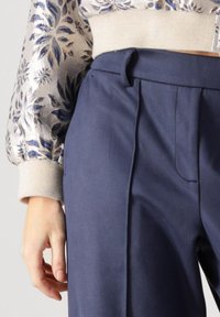 Marineblauwe op maat gemaakte broek met voorplooien, met een soepele textuur en een riemlus. Gecombineerd met een gestreepte, metallic-zilveren top.