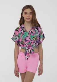 Camicetta nera a maniche corte e corta con vivaci motivi floreali rosa, verdi e viola; abbinata a pantaloni corti di denim rosa con risvolti.