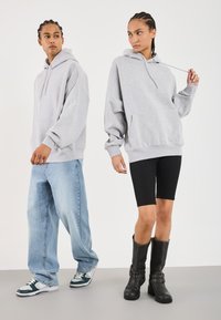 Felpe oversized grigie, jeans larghi blu chiaro e stivali neri al ginocchio. La felpa ha una tasca frontale e un cordino regolabile.