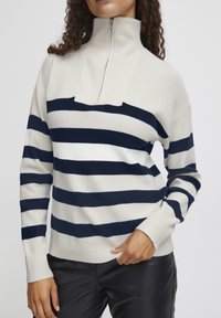 Pull à rayures crème et marine avec un col haut et un design à demi-fermeture éclair. Texture côtelée, silhouette ajustée et manches longues.