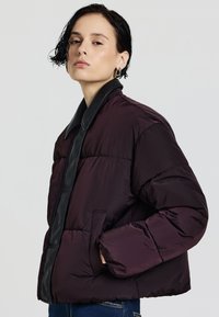 Lila Pufferjacke mit einem glänzenden schwarzen Kragen und seitlichen Taschen. Sie verfügt über eine kastige Form und eine gesteppte Textur, ideal für lässige Anlässe.