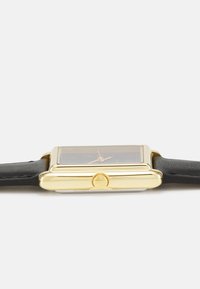 Montre rectangulaire en or avec un bracelet en cuir noir, dotée d'un verre clair et d'une couronne ronde sur le côté pour régler l'heure.