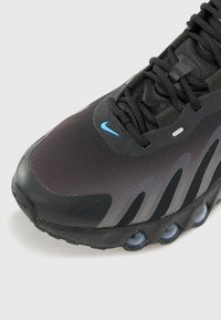Schwarzer und grauer Sportschuh mit Mesh-Obermaterial, geschwungenem Design, blauen Akzenten und sichtbaren Luftkissen in der Sohle.