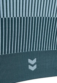 Gebreid textiel met afwisselend lichtblauwe en teal verticale strepen, met ribbeltextuur en een wit logo aan de onderrand.