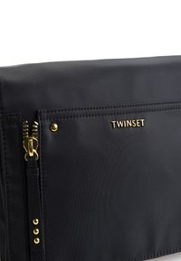 Borsa in nylon nera con una texture liscia, dettagli in metallo dorato, tasca anteriore con zip e logo "TWINESET" in lettere dorate.