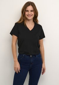 Černé tričko s V výstřihem vyrobené z měkké bavlny, s krátkými rukávy a volným střihem. V kombinaci s tmavě modrými džíny.