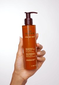 Bärnstensflaska med ett brunt pump-lock, märkt "Nuxe rêve de miel" i guld. Innehåller 200 ml ansiktsrengöringsgel med honung och solros.