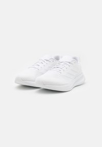 Sneakers bianchi da ginnastica con tomaia in rete, chiusura con lacci, design a tre strisce sui lati e suola in gomma bianca texturizzata.