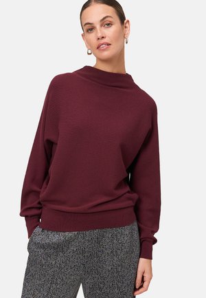 Pull-over en ribbed bourgogne avec un col montant, coupe décontractée et manches longues, associé à un pantalon gris à motifs.