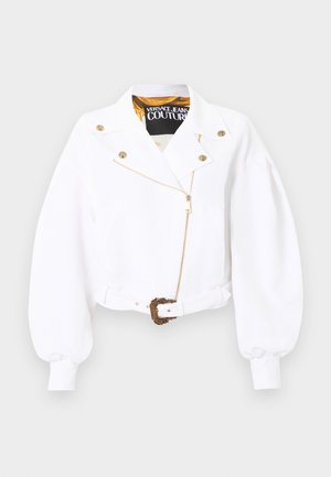 Veste blanche courte avec manches bouffantes, fermeture éclair et boutons dorés, taille ceinturée avec une boucle ornée en or, étiquette Versace Jeans Couture à l'intérieur du col.