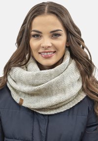 Écharpe en tricot beige en forme d'infini avec un motif texturé et un léger éclat, arborant une petite étiquette en cuir marron d'un côté.