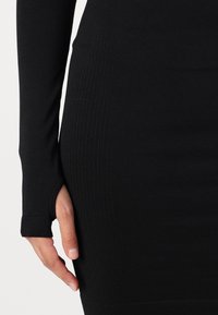 Melna garām piedurknēm kleita ar ribotu tekstūru, ar izgriezumu īkšķa cauruma detaļu piedurknē un pieguļošu piegriezumu. Mīksts audums.