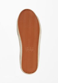 Semelle de chaussure en caoutchouc avec un motif chevrons orange. Logo "GUESS" embossé près de la voûte plantaire. Bordure latérale blanche autour du contour.