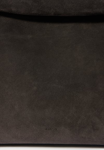 Tumši brūna velveta ādas rokassoma ar smalki reljefu logotipu netālu no apakšējā centra, attēlota pret vienkāršu fonu.