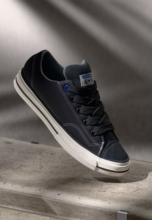 Schwarze Leinensneaker mit blauen Ösen, weißer Gummisohle und strukturiertem Zehenbereich. Verfügt über kontrastierende Nähte und ein "All Star"-Logo-Patch.