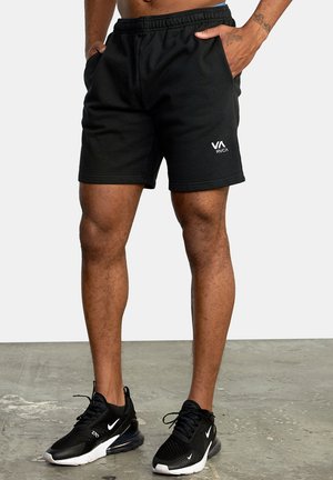 Black athletic shorts with an elastic waistband and side pockets, featuring a white RVA logo on the front. Worn with black sneakers.