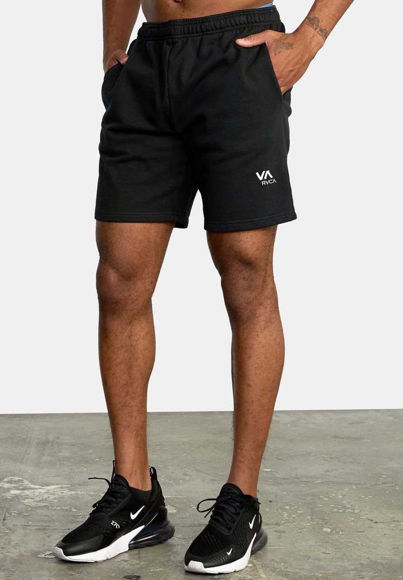 Black athletic shorts with an elastic waistband and side pockets, featuring a white RVA logo on the front. Worn with black sneakers.