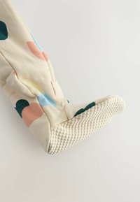 Miękkie kremowe pajacyki dla niemowląt z stopami, zdobione wielokolorowymi abstrakcyjnymi wzorami oraz teksturowaną, antypoślizgową podeszwą na białym tle.