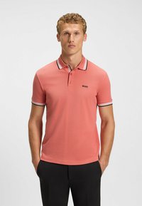 Pikétröja i korall med en strukturerad yta, treknapps placket och en kontrasterande krage och ärmar i svart och vitt randigt mönster.