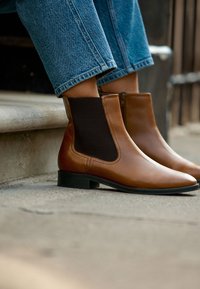 Bottines en cuir marron avec panneaux latéraux élastiques, bout arrondi élégant et petits talons carrés, portées avec un jean en denim.