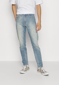 Light blue denim jeans with a slim fit and faded texture. Paired with black and white zebra-patterned sneakers. White t-shirt visible above.
