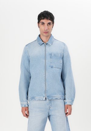 Light blue denim jacket with a front zip, pointed collar, and a single chest pocket. Features stitched detailing and long sleeves.
