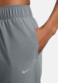 Grijze sportkorte broek met een elastische tailleband, voorzien van een zijzak en een subtiel wit Nike-logo op de zoom. Gladde stoftextuur.