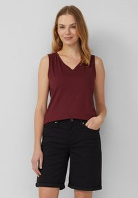 Bordeaux mouwloos topje met een V-halsontwerp, gecombineerd met knielange zwarte shorts met opgerolde manchetten en zijzakken.