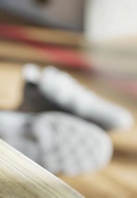 Nello sneakers sono parzialmente visibili sullo sfondo, con una superficie di legno in primo piano. Il legno ha una texture liscia e una leggera venatura.