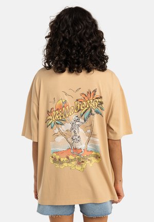 Beige oversized t-shirt med grafik af et skelet blandt palmer, med solnedgang og blomsterdetaljer nederst.