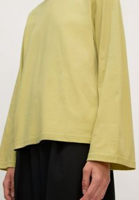 Lange mouwen, lichtgele blouse van zachte stof met een relaxte pasvorm; afgeronde hem en brede mouwen, gecombineerd met zwarte, losse broek.