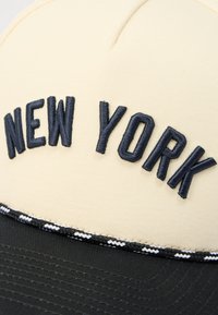 Kšiltovka s krémovou korunkou, černým kšiltem, černo-bílým pleteným lemováním, nápis "NEW YORK" vyšitý černě na předním panelu.