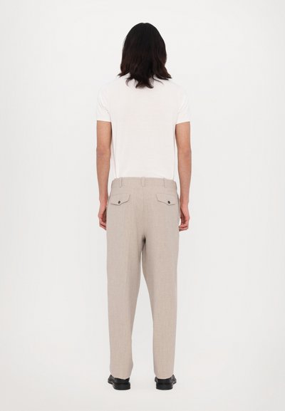 Pantalon en lin gris clair à jambes droites, doté de deux poches arrière et de boutons noirs. Porté avec une chemise blanche unie à manches courtes.
