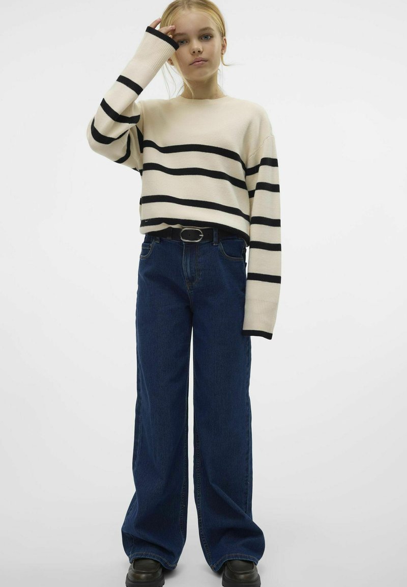 Pull rayé en crème et noir, coupe décontractée, associé à un jean en denim bleu taille haute et jambes larges, avec des chaussures à plateforme noires.