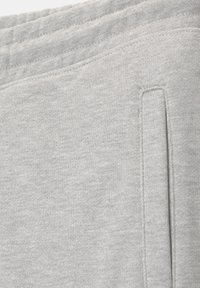 Gros plan du tissu gris clair d'un pantalon de survêtement montrant la ceinture élastique et le détail de la couture verticale de la poche latérale.